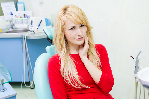 Blonde woman in dental chair grabbing her jaw in pain and the dentist will speak to her about bruxism at Lanier Valley Dentistry in Dacula, GA 