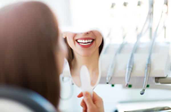 Woman looking at her smile in a mirror from Lanier Valley Dentistry in Dacula, GA